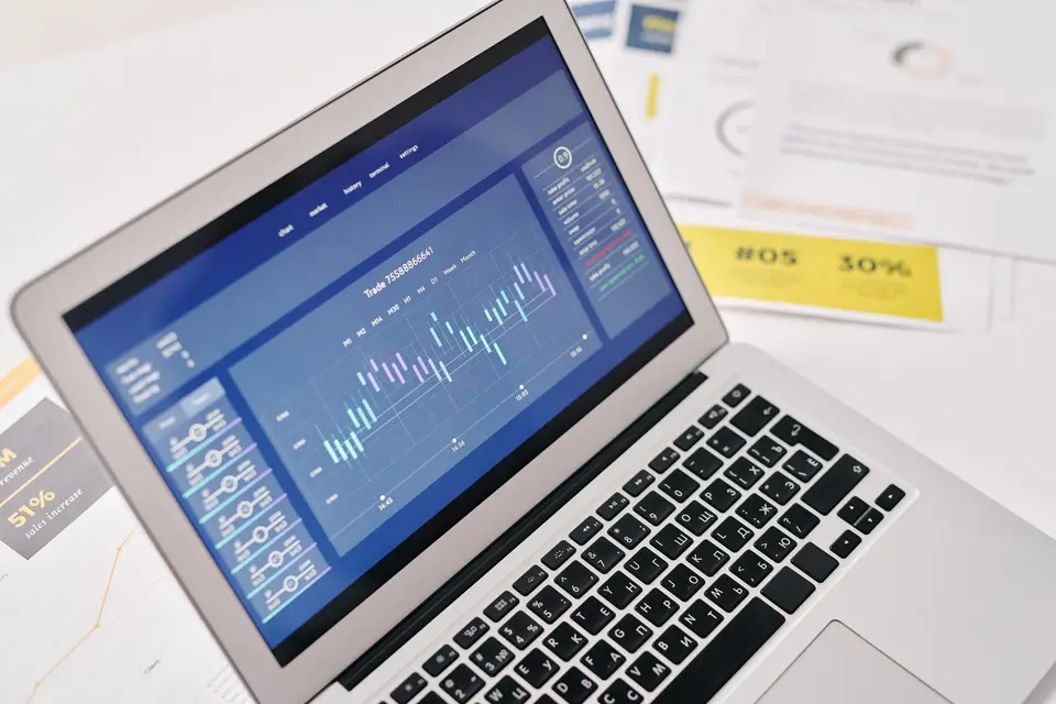Laptop mit Finanzdiagrammen neben Unterlagen auf einem Schreibtisch