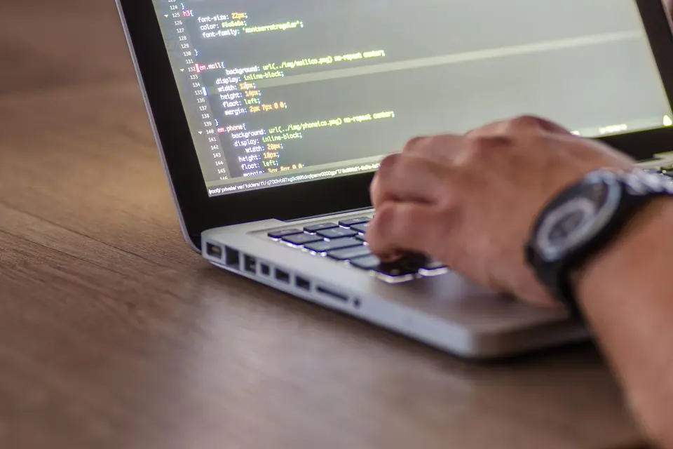 Hände auf einer Laptoptastatur, auf dem Bildschirm Quellcode