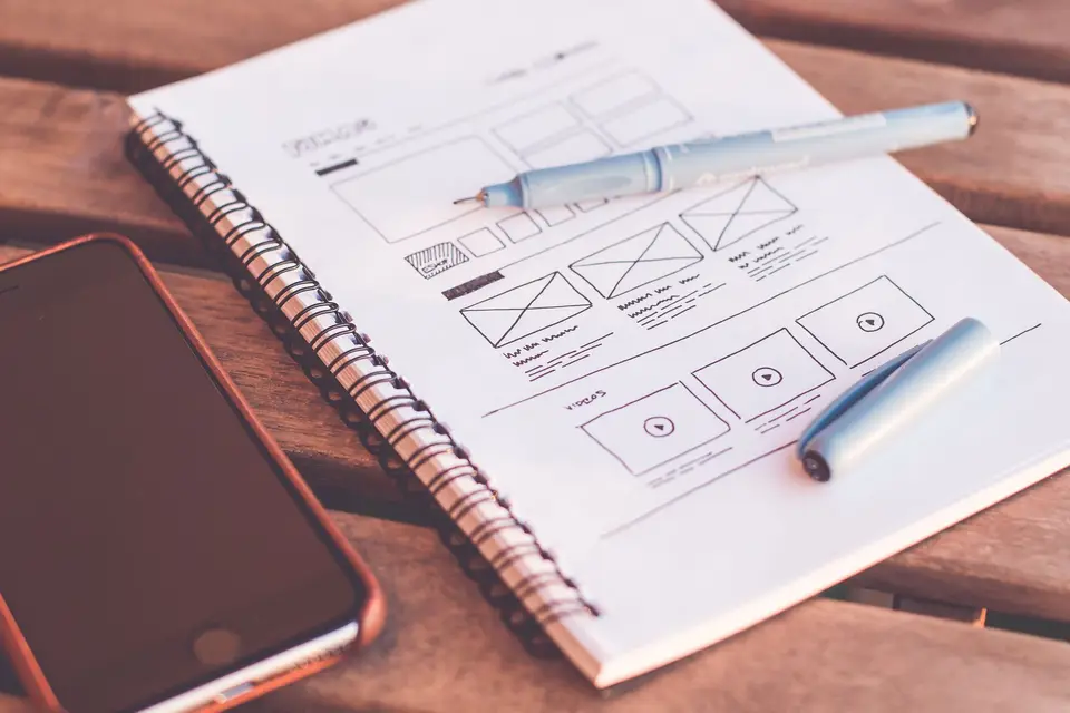 Notizbuch mit Wireframe-Skizzen, daneben Stift und Smartphone